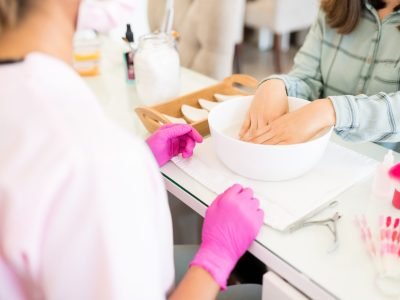 Employee servicing female client with hands in bowl at nail salon