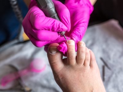 Pedicurist master in pink gloves cuts the cuticle and shellac toe nails in the pedicure salon using drill.  Professional pedicure in cosmetology clinic. Hygiene for feet in beauty salon.